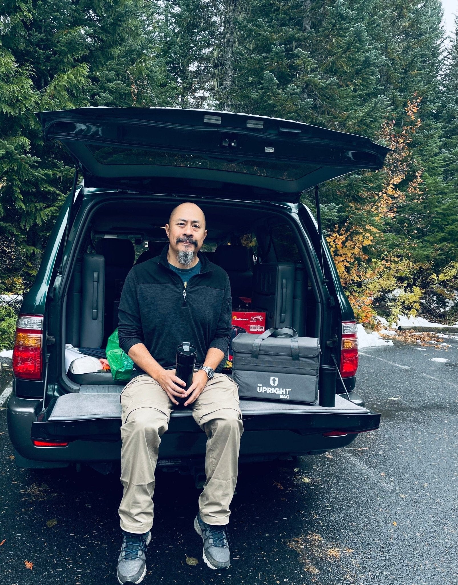 Man sitting in the open trunk of a black SUV with a thermal delivery bag.